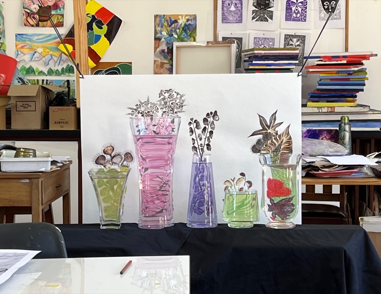 The developed botanical piece — the same five plant arrangements now set inside coloured glass vases — propped on an easel in a busy art studio, with other students' paintings stacked behind it.